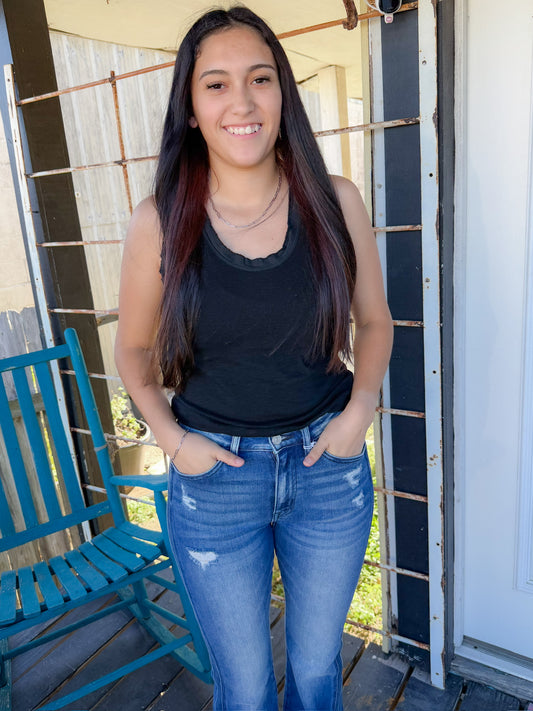Woman wearing a black tank top and blue jeans standing on a porch.