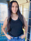 Woman wearing a black tank top and blue jeans standing outdoors.