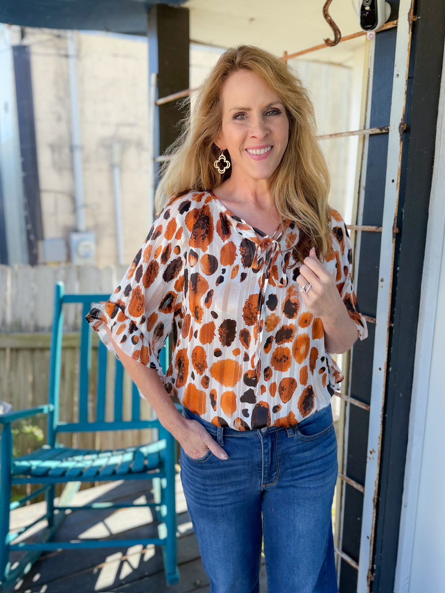 Woman wearing a patterned blouse and jeans on a porch