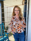 Woman wearing a patterned blouse and jeans standing on a porch.