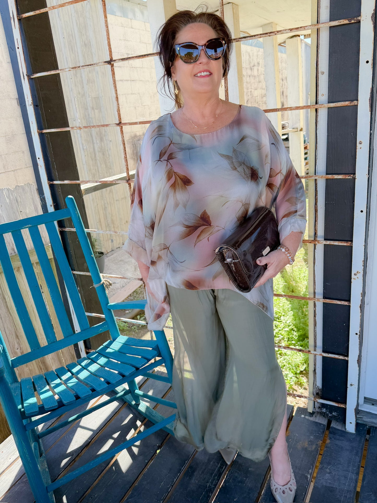 Woman standing on a porch with a blue chair and wooden railing.