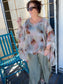 Woman wearing a floral blouse and light pants on a porch with a blue chair.