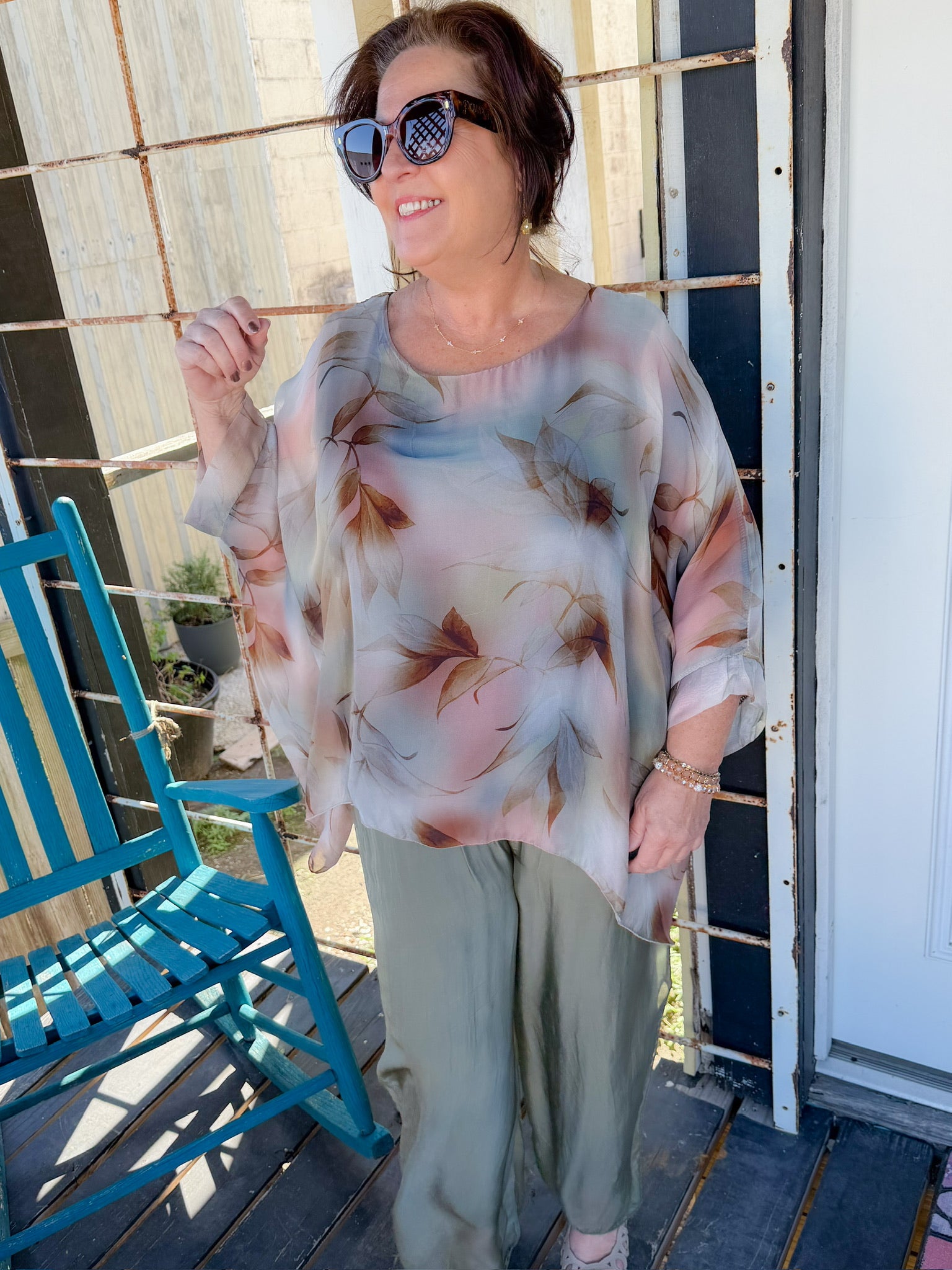Woman wearing a floral blouse and green pants on a porch.