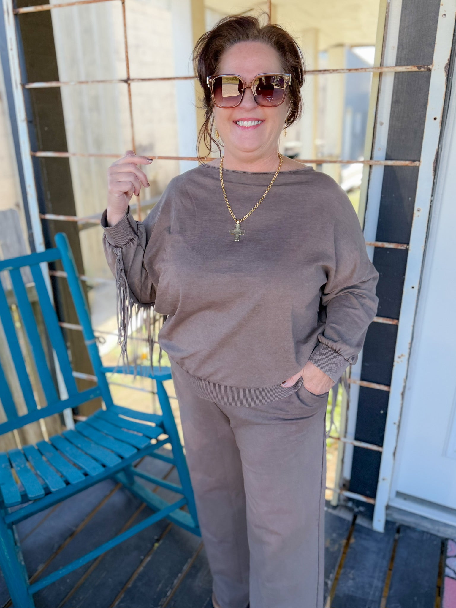Woman wearing a brown outfit on a porch with a blue chair and white door.