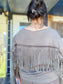 Person wearing a beige fringe cardigan with a blurred background