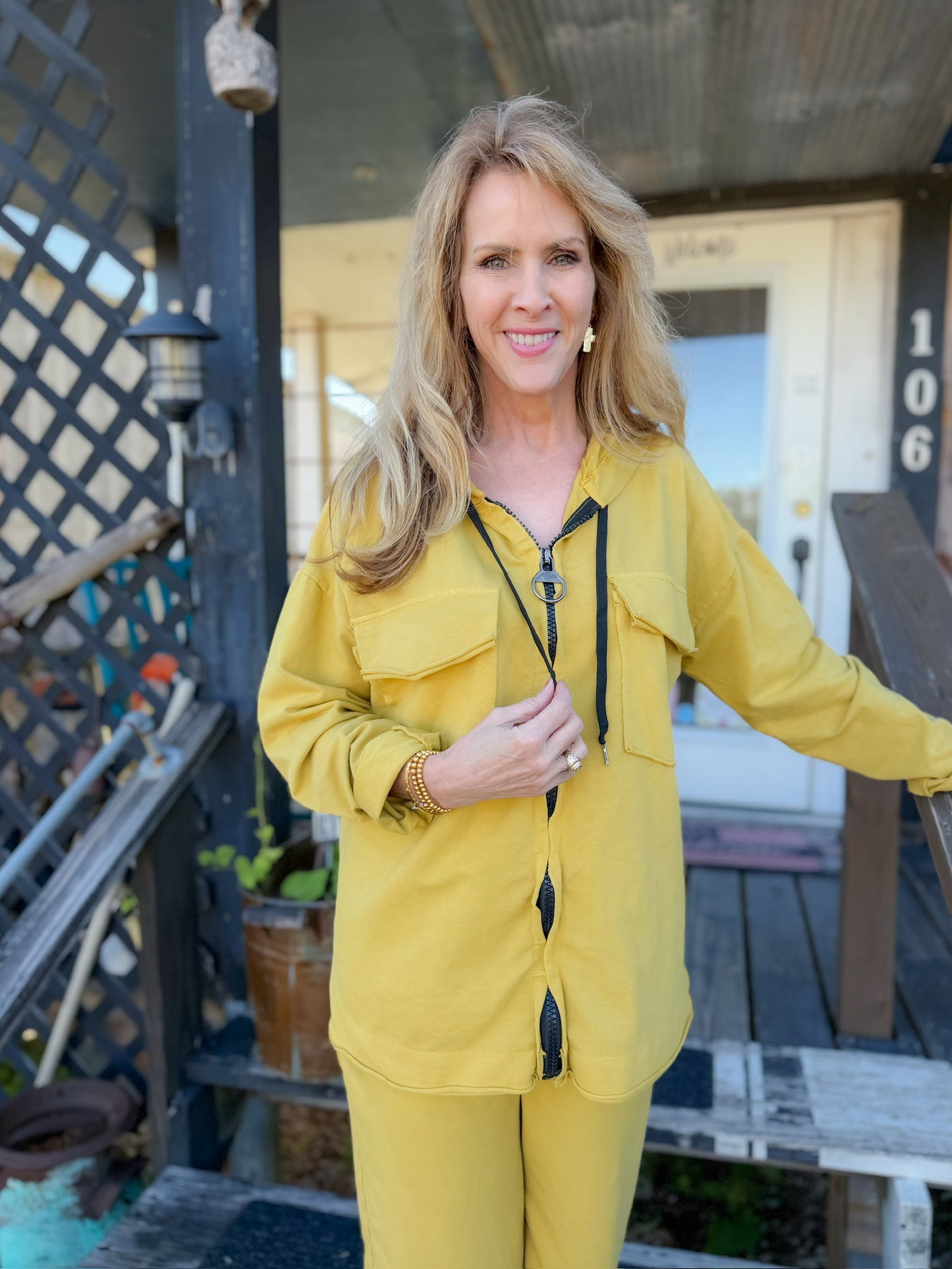 Woman in a yellow outfit standing on a porch with a house number '106' in the background.