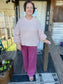 Woman in a pink sweater and purple pants standing on a wooden porch.