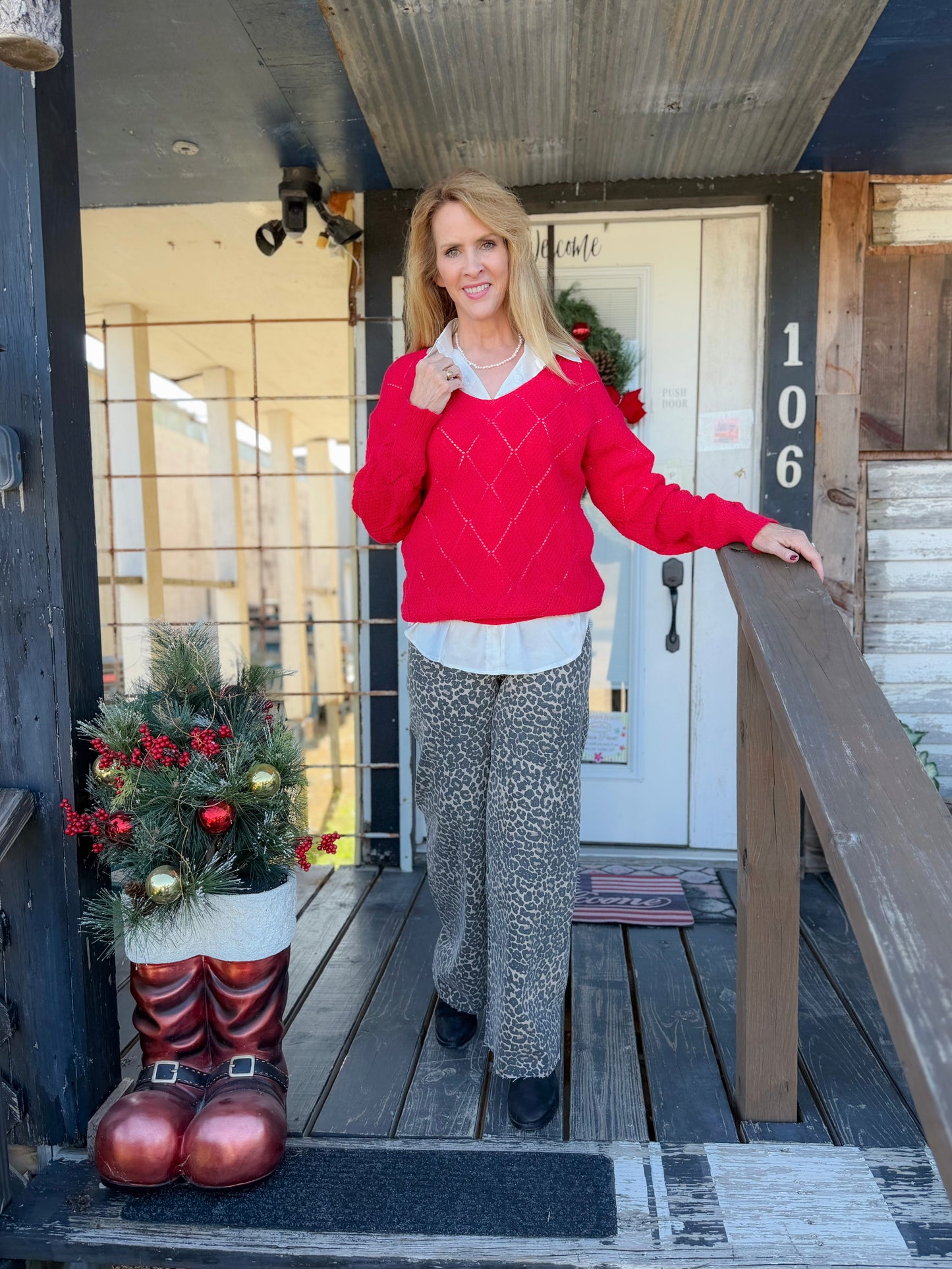 Woman in a red sweater standing on a porch with Christmas decorations.