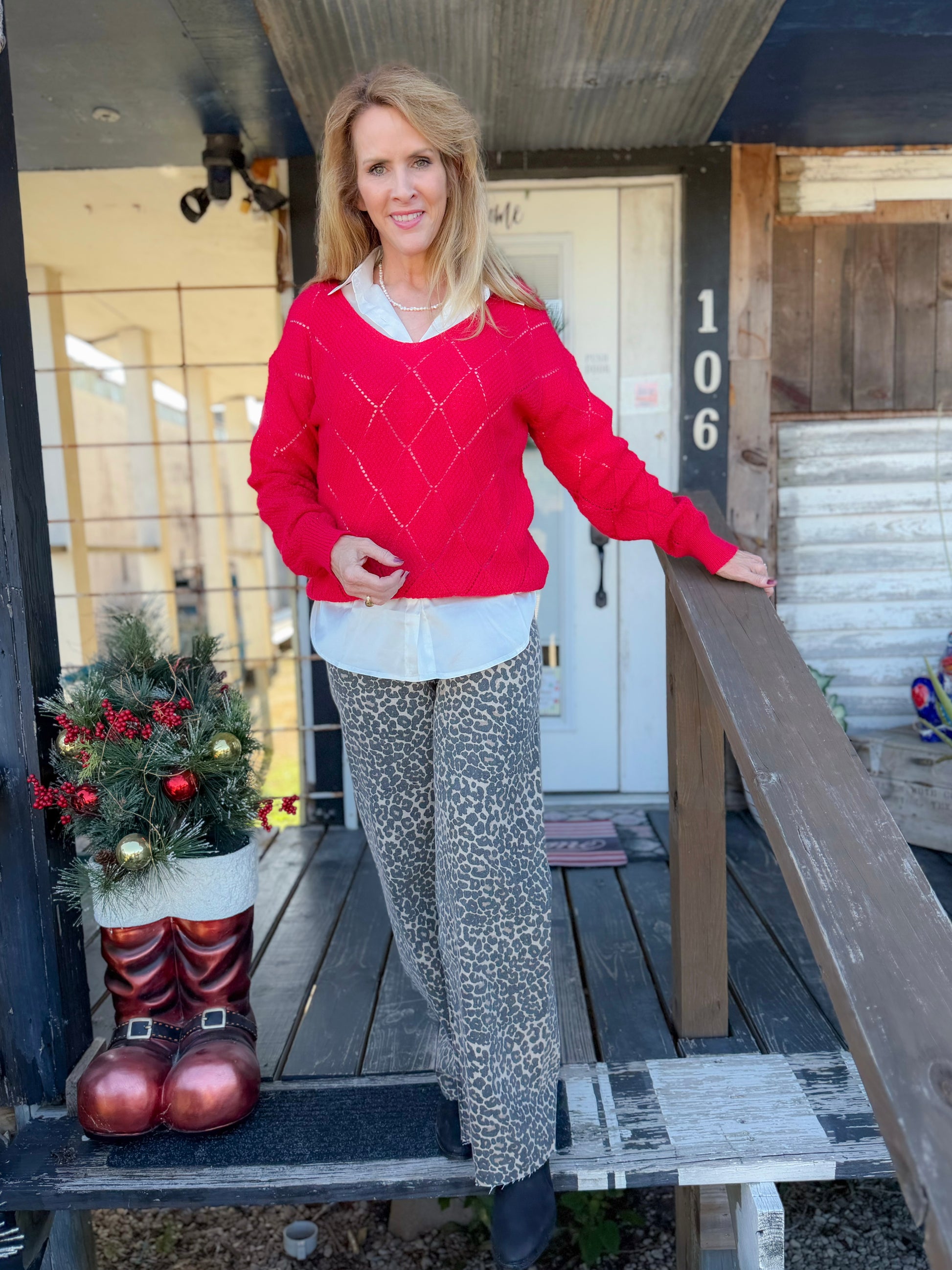 Woman in a red sweater standing on a wooden porch with Christmas decorations.
