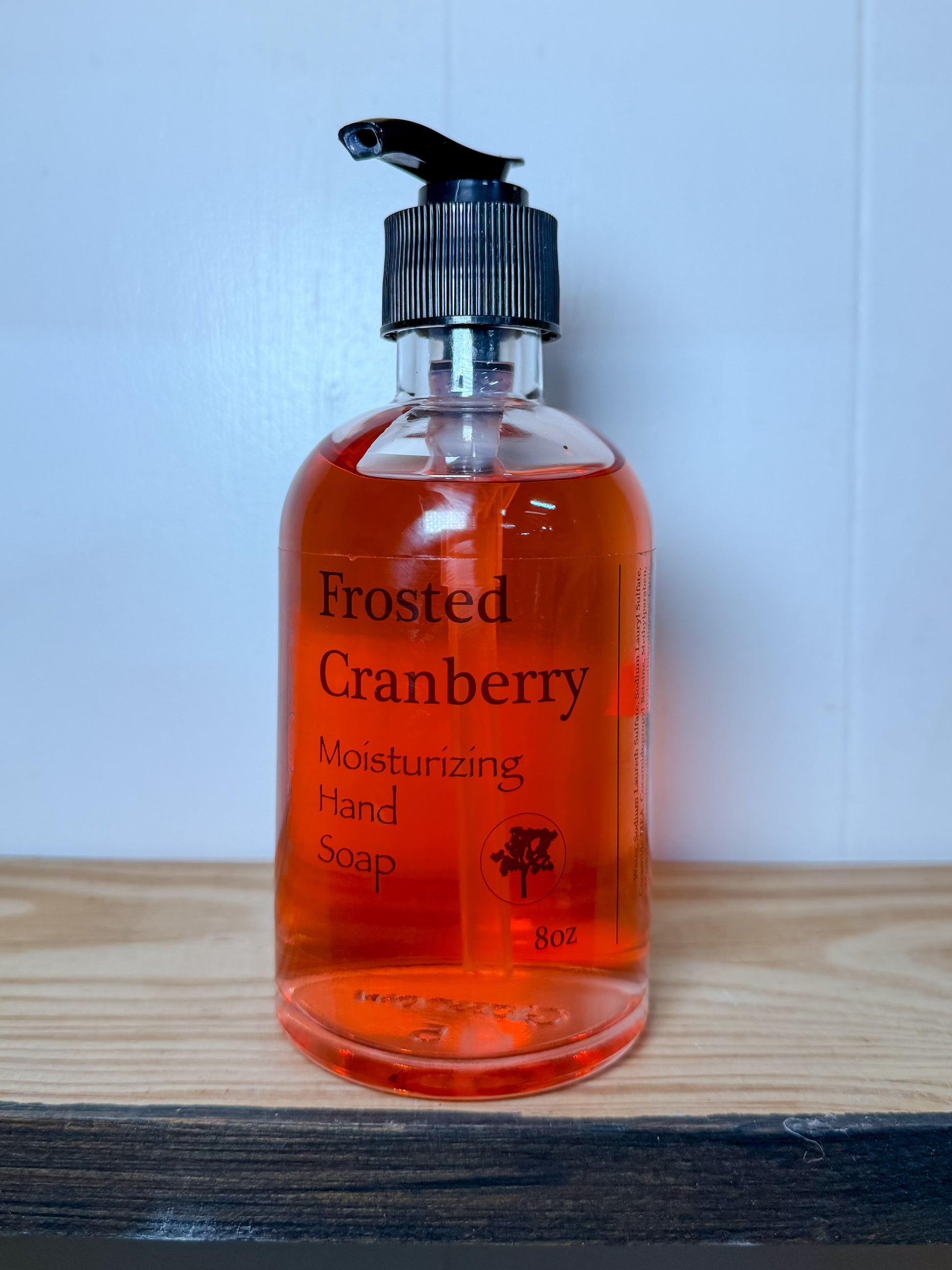 Bottle of Frosted Cranberry hand soap on a wooden surface with a white background