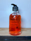 Bottle of Frosted Cranberry hand soap on a wooden surface with a white background