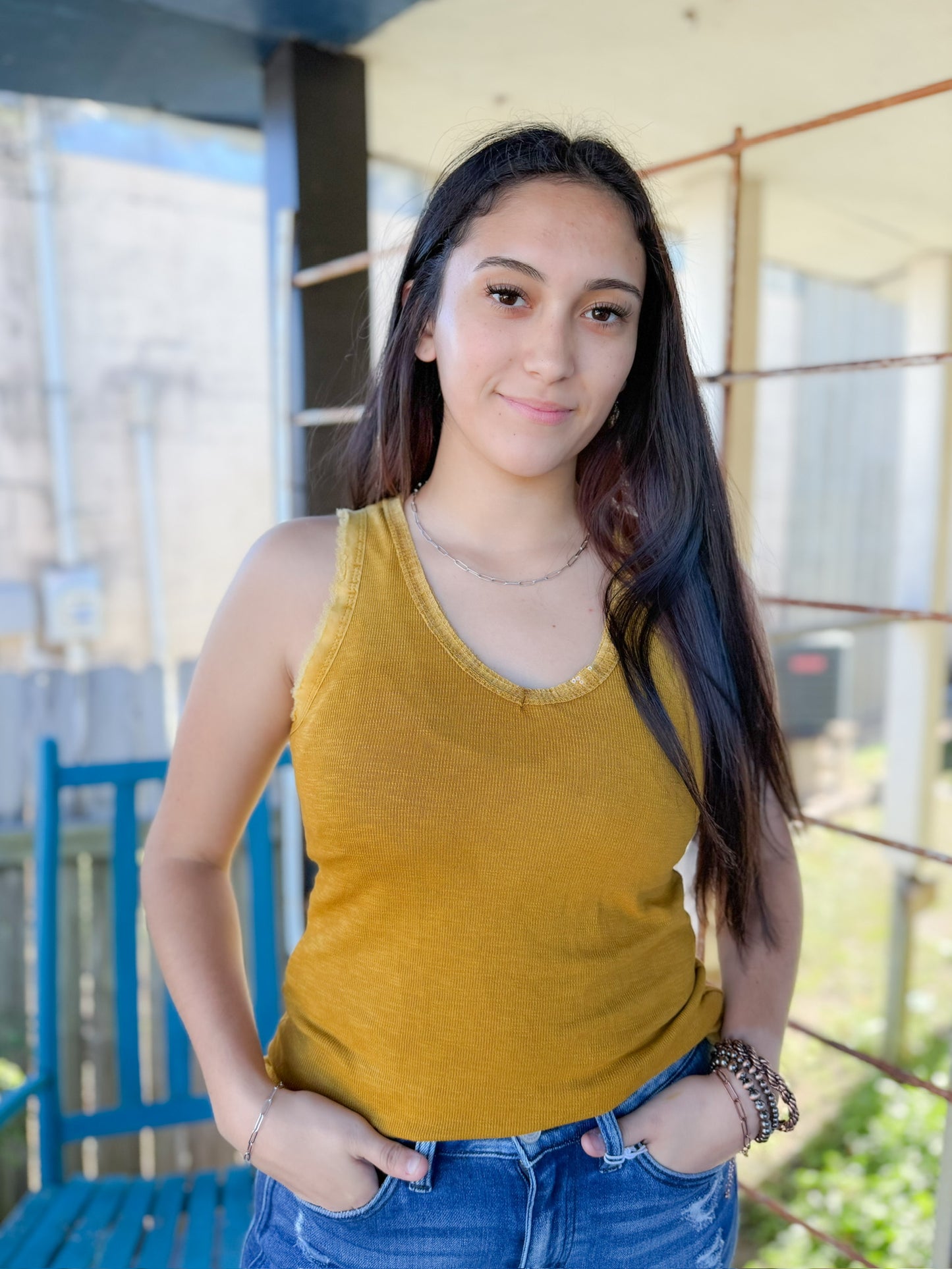 Woman wearing a yellow tank top and blue jeans standing outdoors.