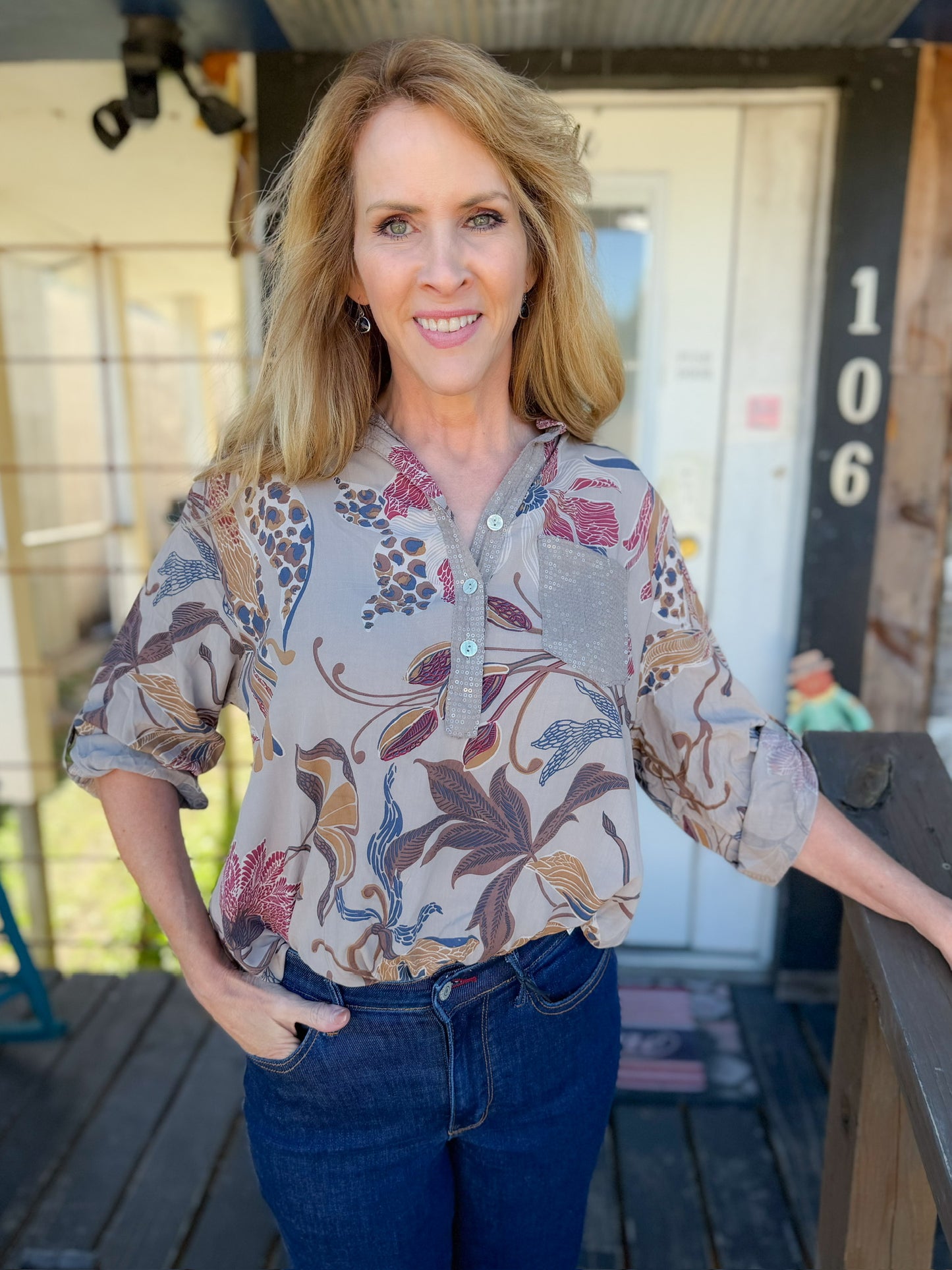Woman wearing a patterned blouse and jeans standing outdoors.