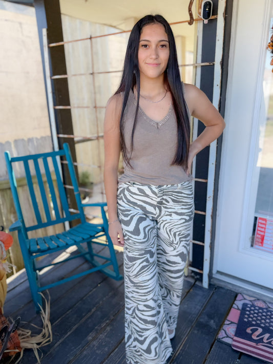 Woman standing on a porch wearing a tank top and zebra print pants.
